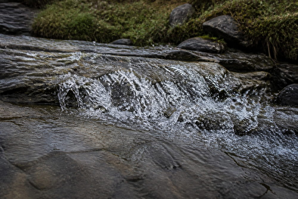 Illustration générée : un ruisseau sous un ciel couvert, ses éclaboussures figées dans l'air, tel que le rendent f/2.8, 1/1000, ISO 800 à 24 mm